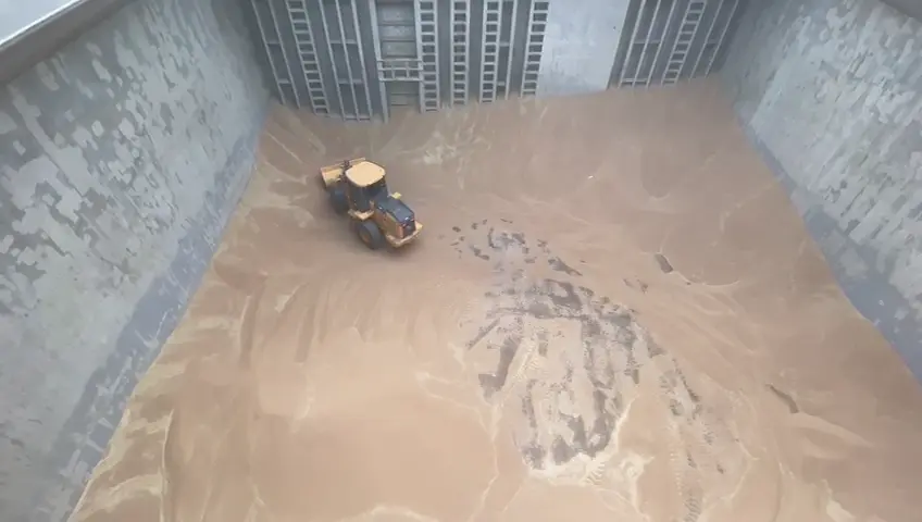 Vídeo aéreo da pá carregadeira John Deere 524 organizando carga de malte no porão de um navio